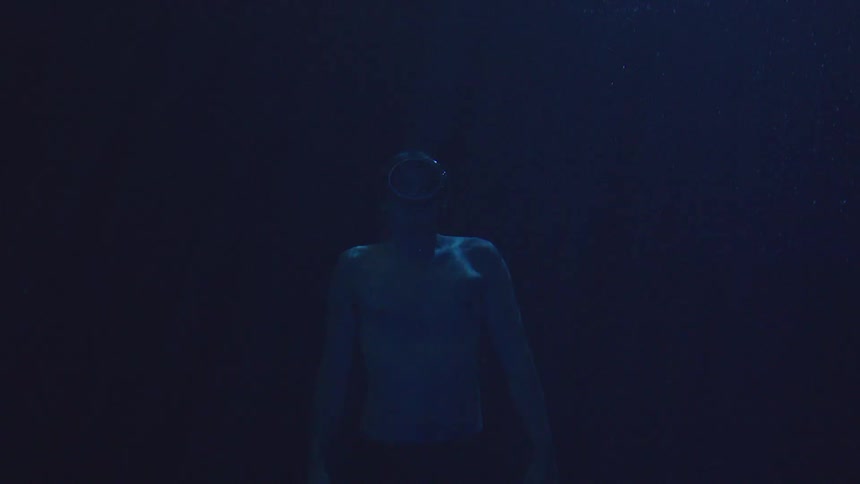 Person underwater looks toward the illuminated blue beam in the stillness of the water