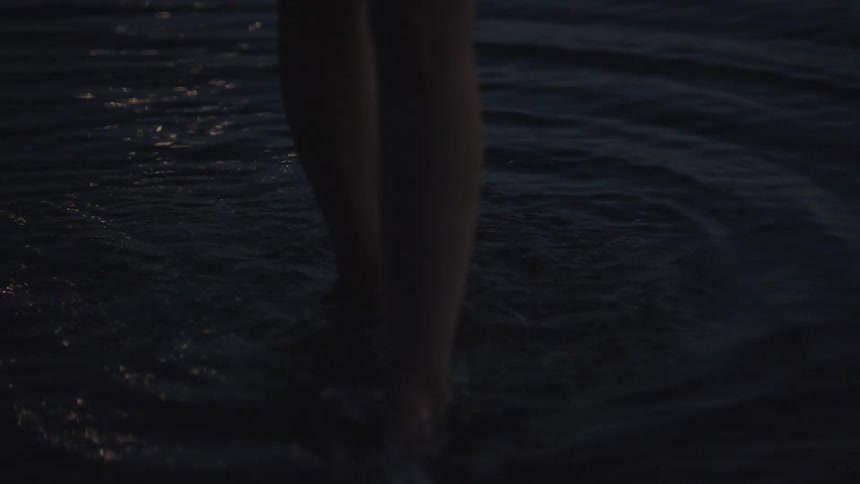 Feet walk slowly through shallow water at dusk