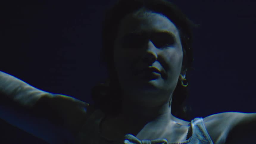 A young woman swims deep underwater holding her breath as she glides through the calm blue depths with graceful motion
