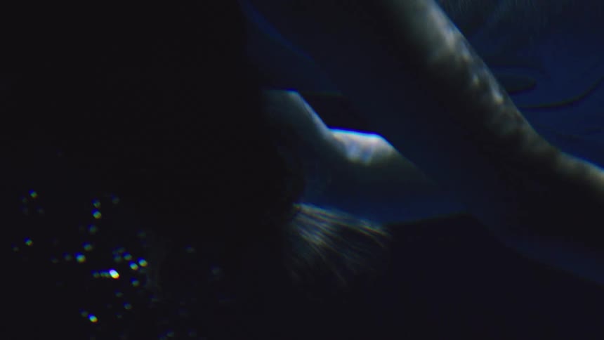 A person is submerged underwater with hair floating and small bubbles rising lit in dim blue tones