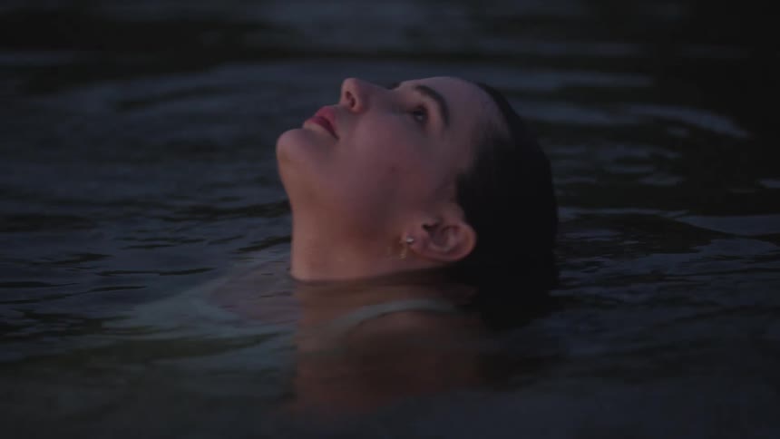 A young woman swims in the ocean at midday wearing a white top as sunlight sparkles across the waters surface and gentle waves surround her
