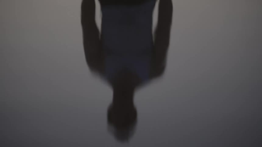 Upsidedown reflection of person standing in sleeveless top over mirrored surface in gray setting