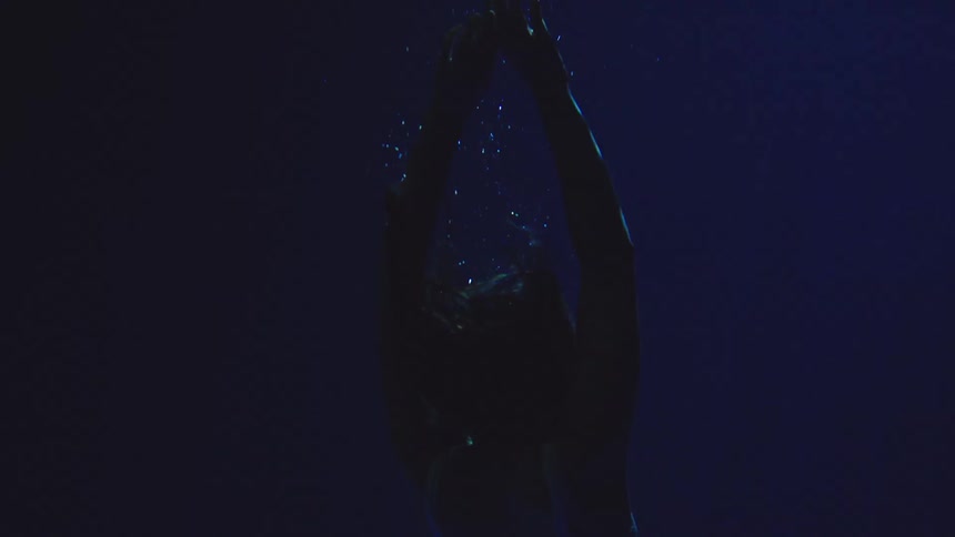 Woman underwater raises her arms as air bubbles rise through the blue water
