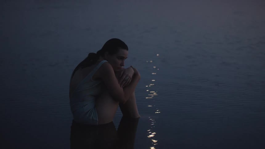 Woman sits in the water hugging her knees under the soft evening light