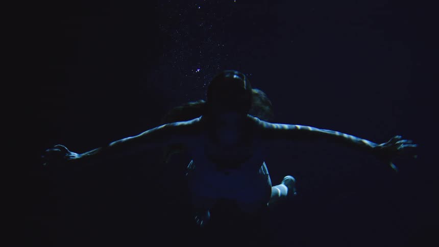 Female person wearing white clothes swimming underwater