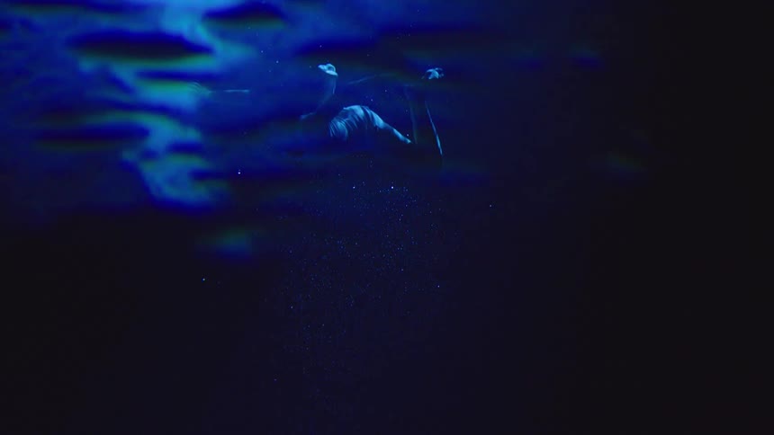 Person submerged in dark water illuminated by blue light