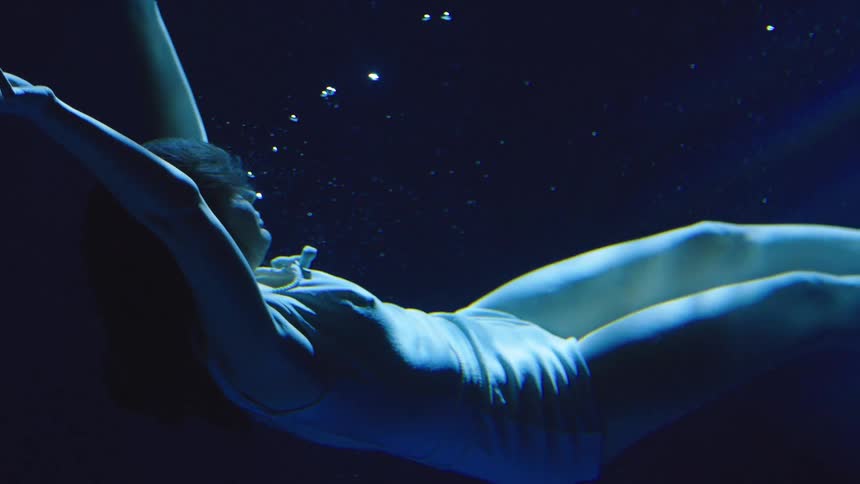 Female person wearing white clothes swimming underwater