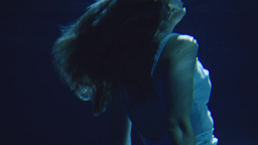 A young woman wearing a white shirt dives gracefully underwater her body slicing through the clear depths as sunlight filters from above casting shimmering patterns around her