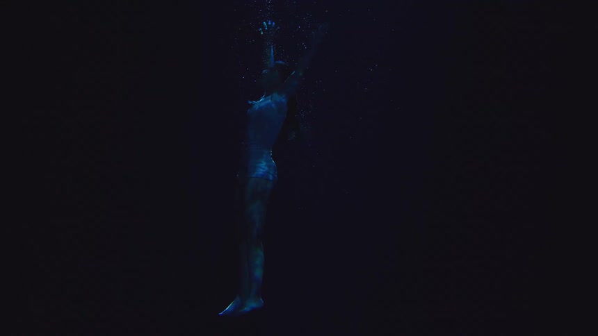 Woman submerged in dark water releases bubbles while floating in silence