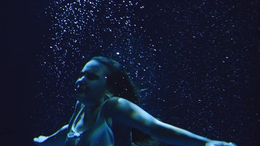 A young woman swims submerged beneath the pool surface her body gliding through the water as bubbles rise and swirl around her in the clea