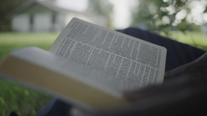 Hand flips through the pages of an open book resting on the lap outdoors