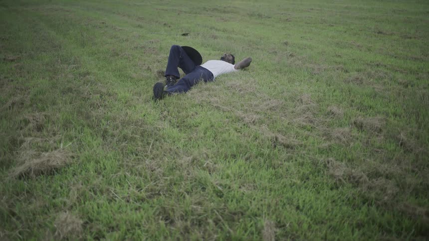 Man with a hat lies on the grass gazing at the sky in an open field
