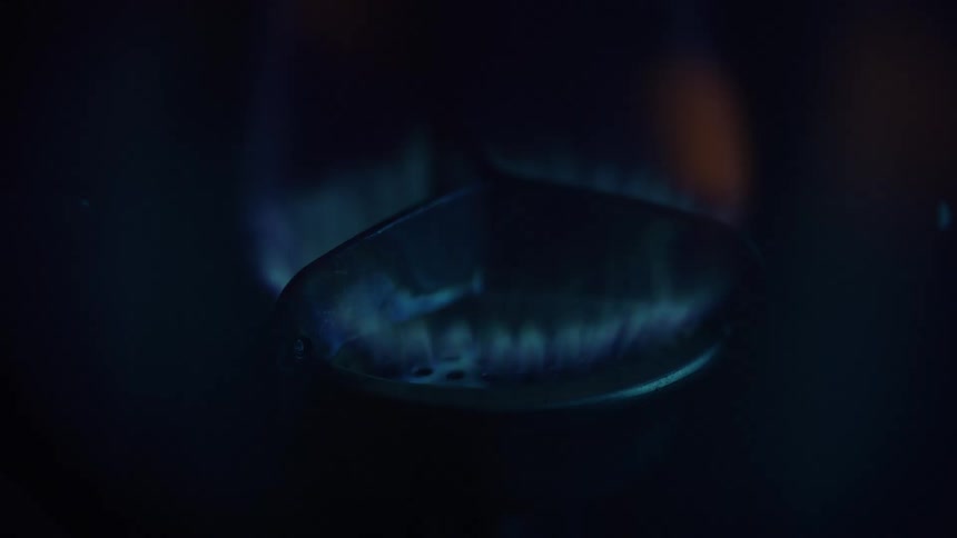 A blue gas flame circles a stovetop burner in darkness