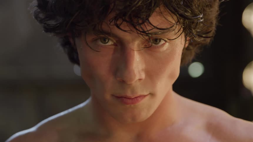 Man stares straight ahead with a serious expression and face lit by warm light