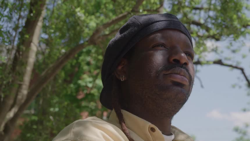 A man in a head wrap looks up outdoors against the bright sky