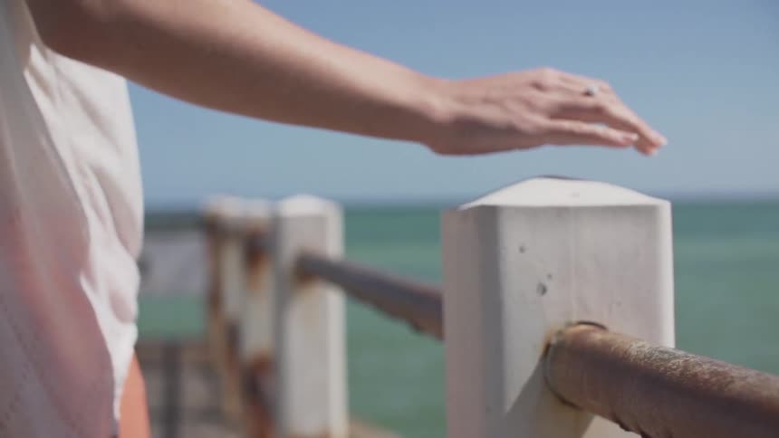 Woman rubs her hand on a beachside fence