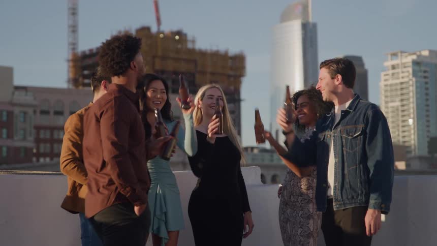Group of friends toast with bottles at sunset on an urban rooftop