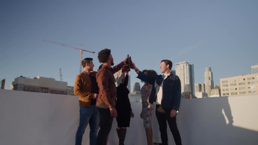 Group of friends toast with bottles on a sunny rooftop in the city