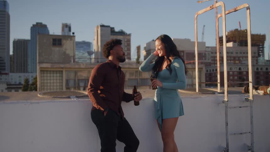 Man and woman chat casually on a rooftop at sunset