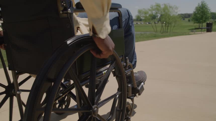 A black man propels his wheelchair along a sunlit path his hand gripping the wheel with steady focus