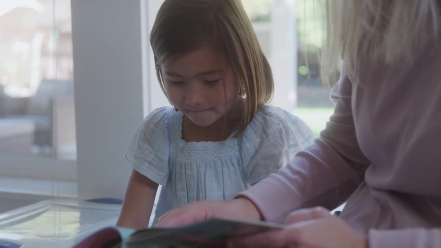 Girl looks closely at a photo album beside a woman