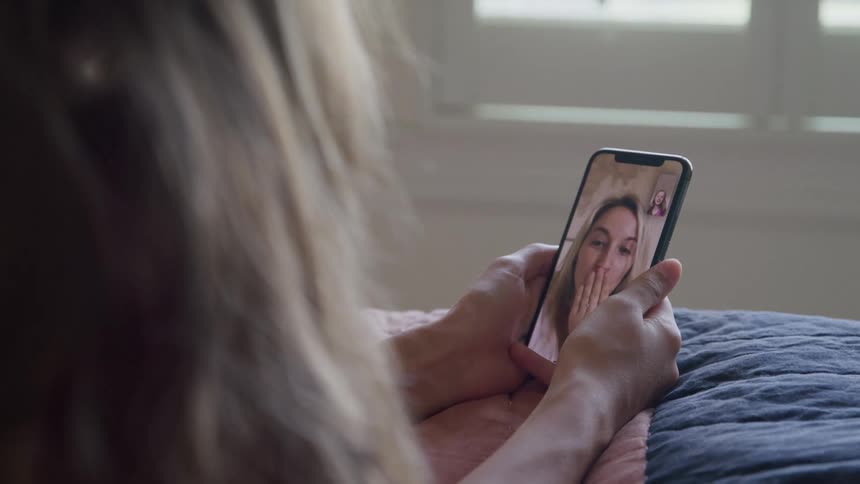 Person holds a phone during a video call with a smiling woman