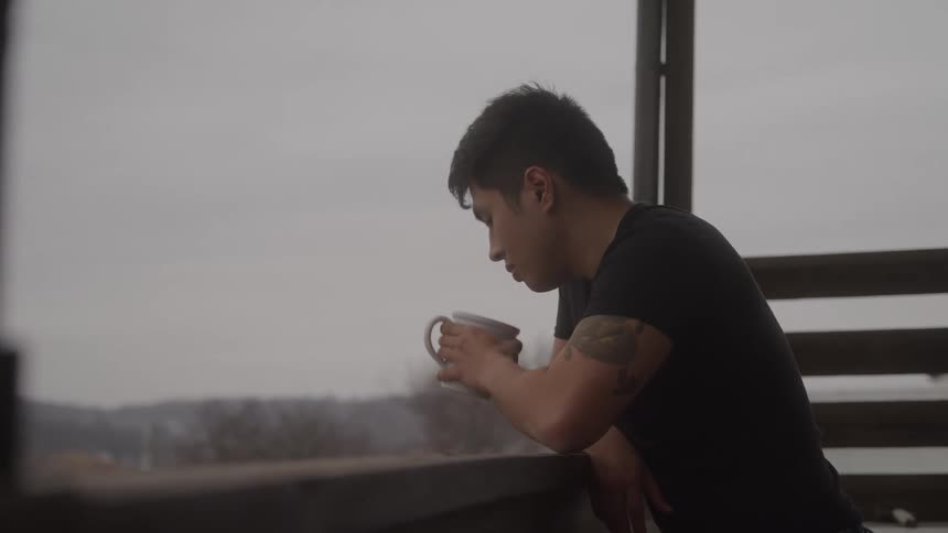 Man leaning on the balcony drinks coffee while watching the cloudy landscape