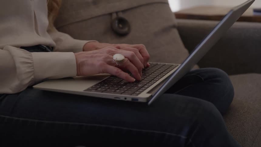 Closeup of hands with a ring typing on a laptop on a sofa
