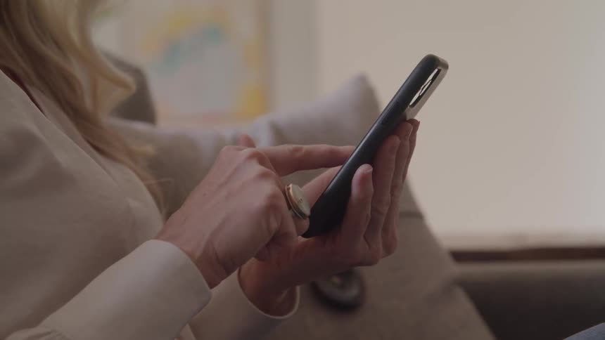 Person seated on couch interacts with smartphone while holding it with one hand