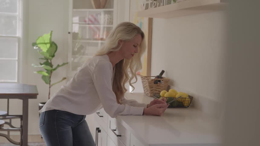 A young woman using a mobile phone while leaning on a counter top in the kitchen during daytime