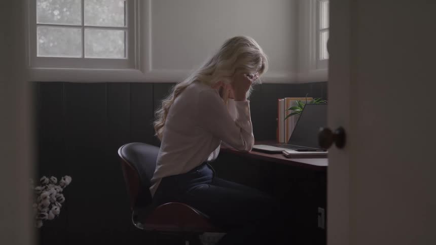 A young blonde woman sitting contemplatively at a desk in an office