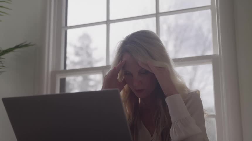 Woman working on a laptop at home on a winter day puts her head on her hands