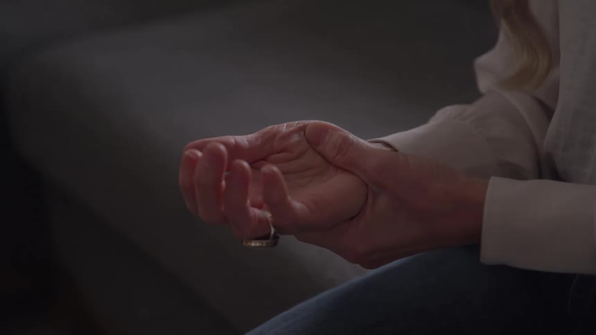In a somber close up a woman slowly unclenches her hands in her lap