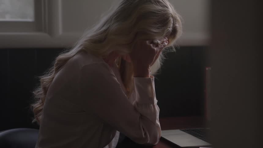 A woman sits with a laptop handling work stress in a dimly lit room