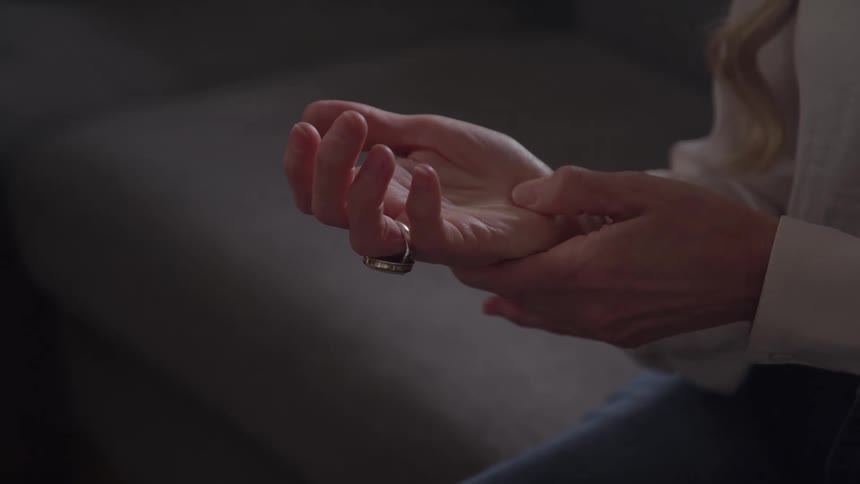 Woman wearing jeans and a white blouse massasing her own hand indoors during day time