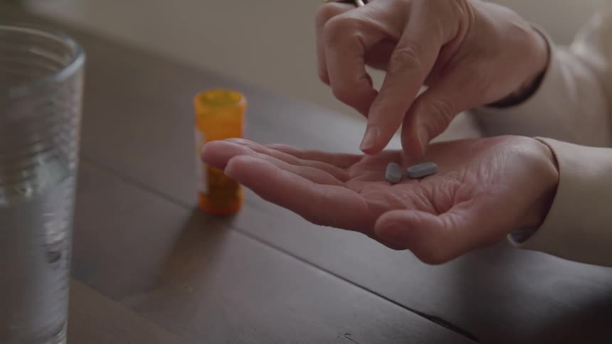 Person holding pills in hand beside a glass of water