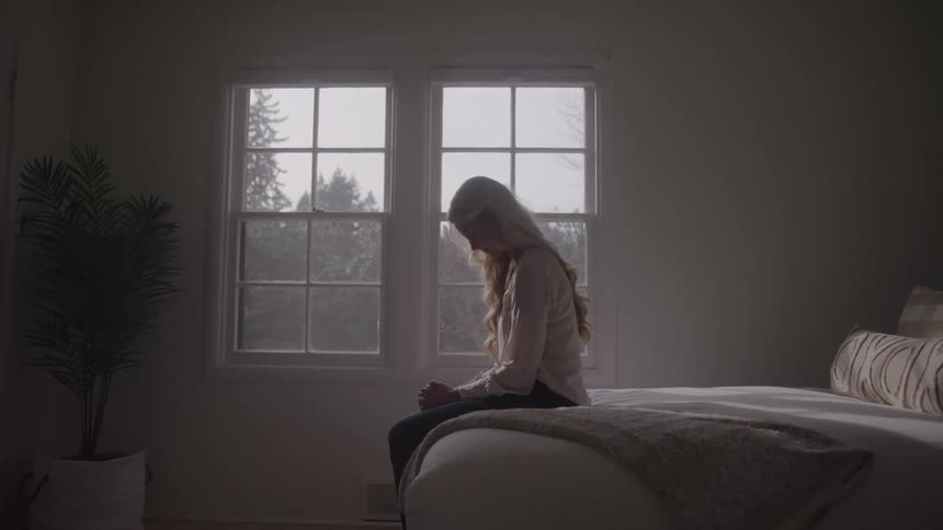 Grieving woman sitting on bed in a dark bedroom