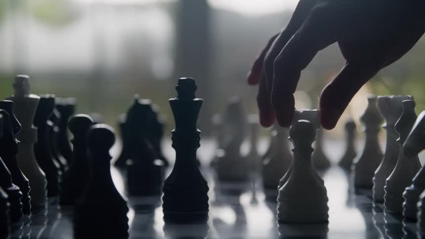 Hand moves white pawn on chessboard lit by natural light highlighting a moment of strategy