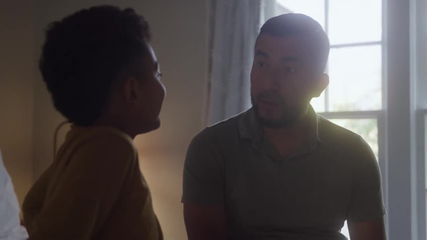 The video shows an intimate moment between a man and a young boy possibly a father and son who are looking and smiling at each other the scene is set indoors near a large window creating a gentle backlighting that highlights their silhouettes