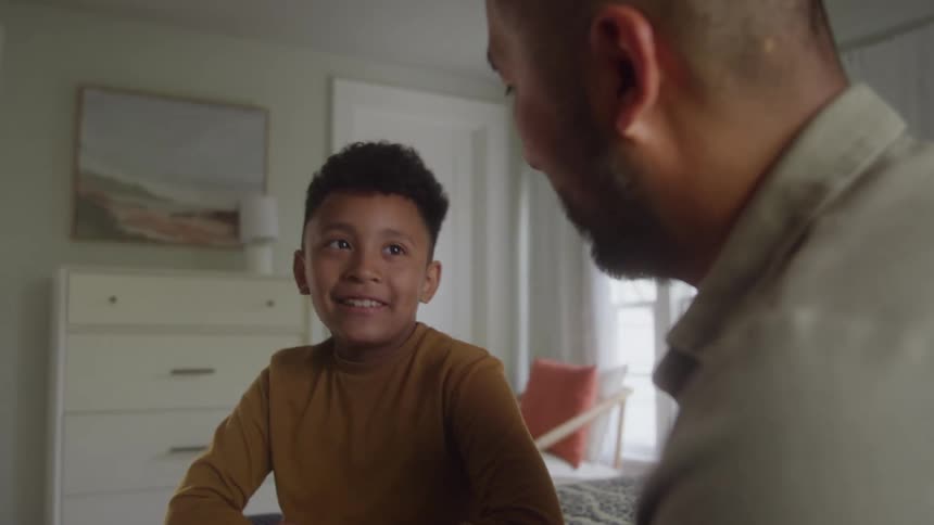 Close up of father and son conversing and celebrating while sitting together on a bed in a bedroom during daytime
