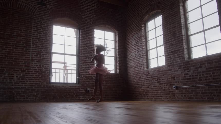 Ballerina spinning gracefully in a brick studio with large illuminated windows