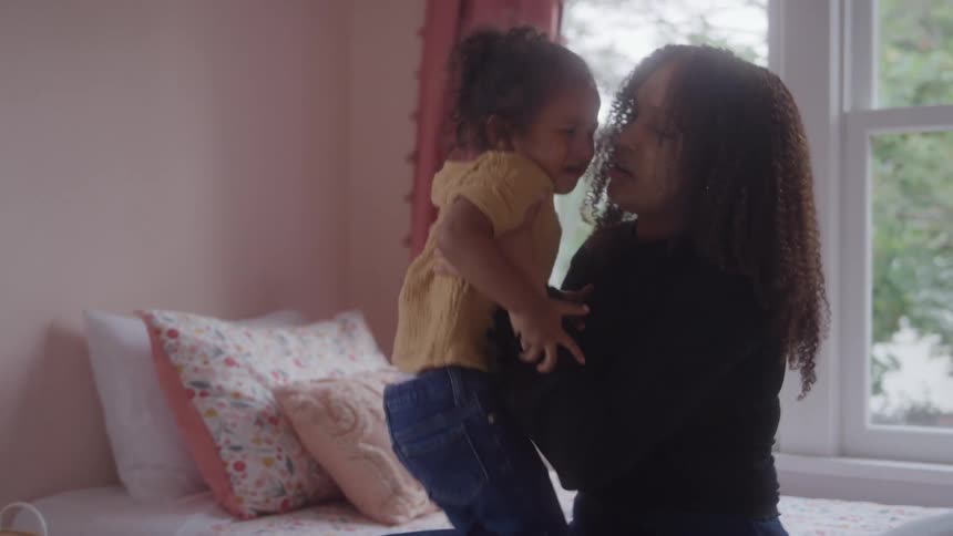 Mother hugging her crying daughter in a room lit by the window