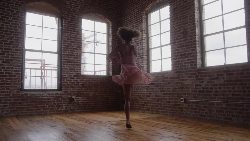 Person performs a dance movement in a spacious room with brick walls and large windows