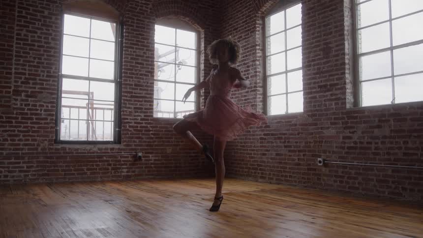 Woman performs ballet spin in a spacious room with wooden floor and exposed brick walls