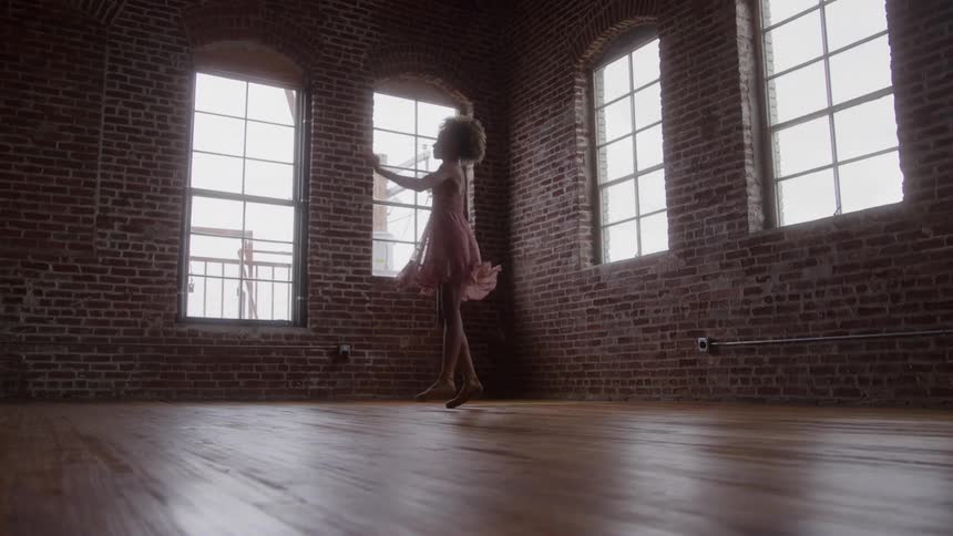 Person dances alone in a studio with brick walls and large windows
