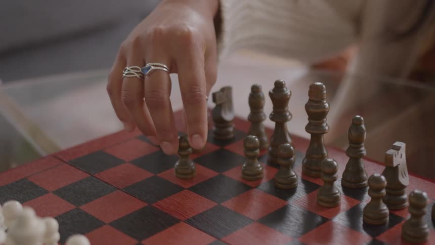 Ringed hand moves metal piece on redandblack chessboard over wooden surface