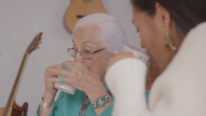 Whitehaired woman with turquoise jewelry drinks from cup