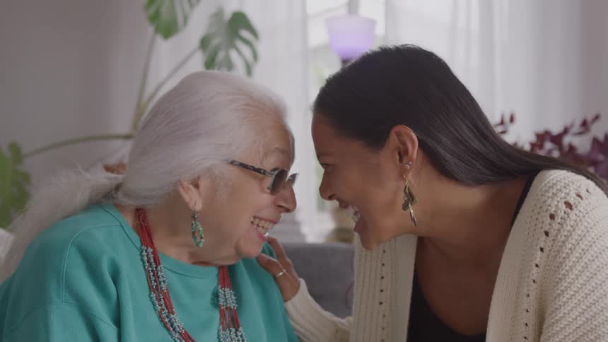 Elderly woman and younger woman smile touching foreheads in a moment of affection