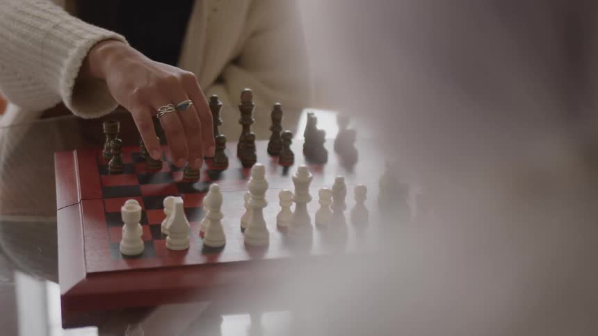 Person in light sweater moves black piece on redandblack chessboard during strategic game