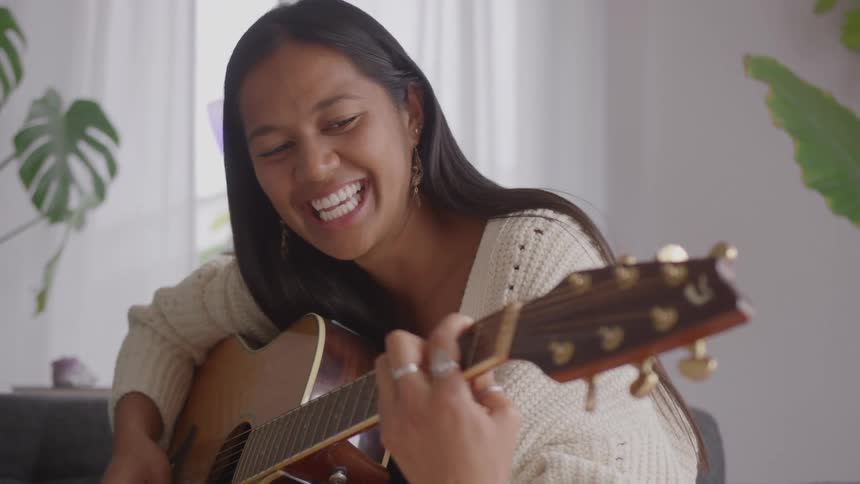 The woman smiles while playing the guitar